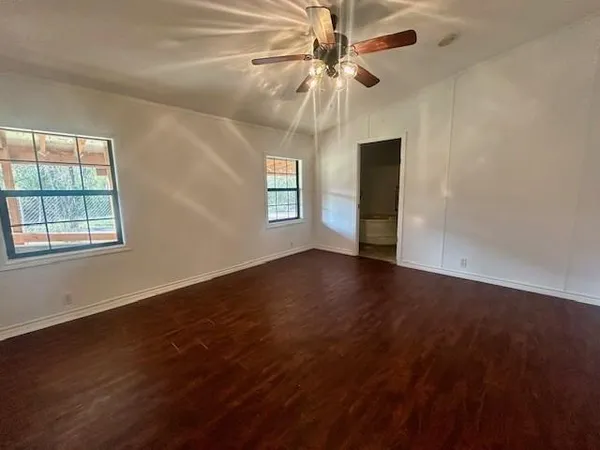 an empty room with wooden floor chandelier fan and windows
