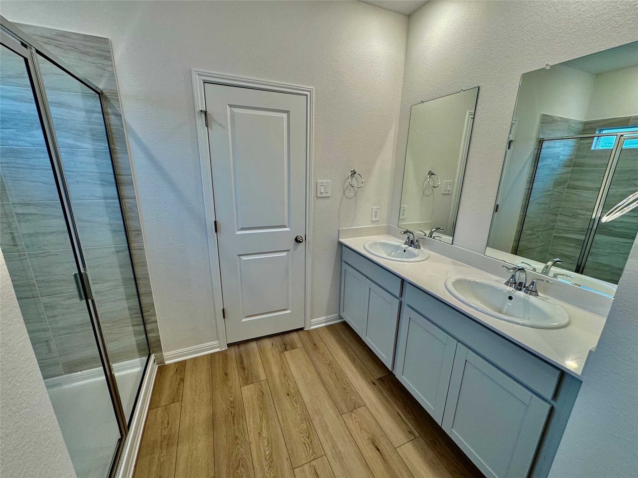 Undisclosed Address Kyle, TX 78640 - Photo 4 of 17 Bathroom featuring a stall shower, light wood-style flooring, double vanity, and a textured wall