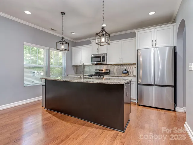 a kitchen with stainless steel appliances granite countertop a refrigerator a sink dishwasher a stove and white cabinets with wooden floor