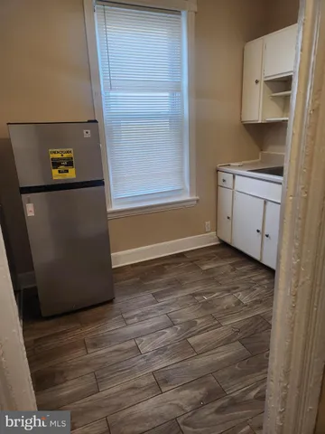a view of a refrigerator in kitchen and an empty room with wooden floor
