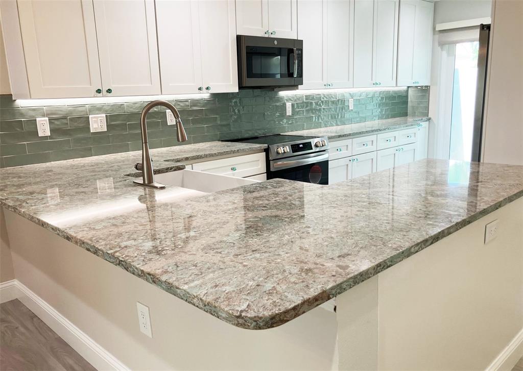 628 Boca Ciega Point Boulevard South St. Petersburg, FL 33708 - Photo 6 of 17 a kitchen with granite countertop a sink a stove and a microwave