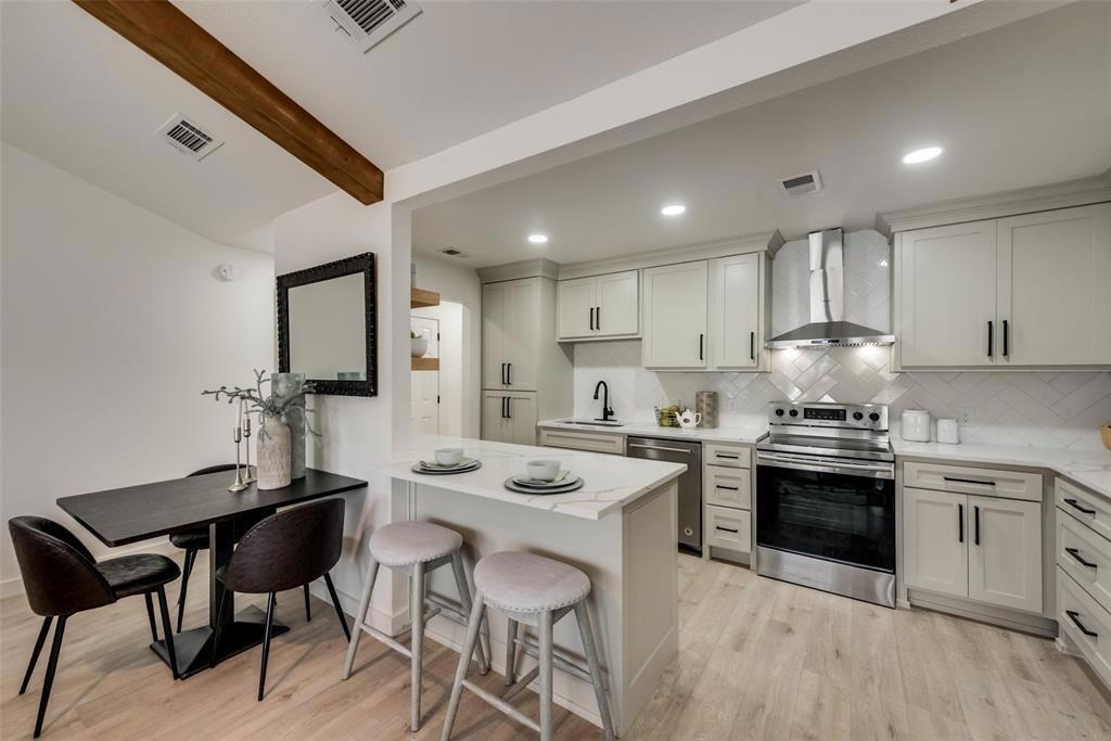 9227 Crimnson Court Dallas, TX 75217 - Photo 4 of 9 Kitchen featuring appliances with stainless steel finishes, beamed ceiling, wall chimney range hood, light wood-style floors, and backsplash