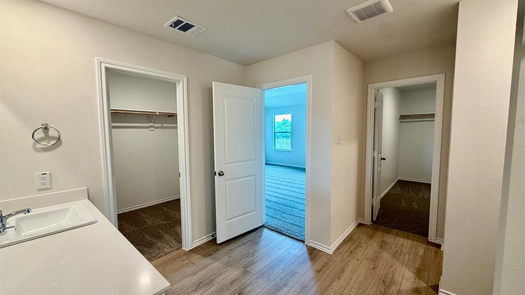 2003 Reveille Way Terrell, TX 75160 - Photo 7 of 25 Hallway with wood-finish flooring, featuring a built-in vanity with an undermount sink and chrome faucet, and two separate closet entries with carpet flooring and clothing rods