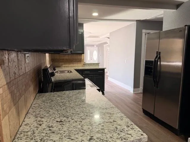 a kitchen with stainless steel appliances granite countertop a refrigerator a stove and a sink with wooden floor