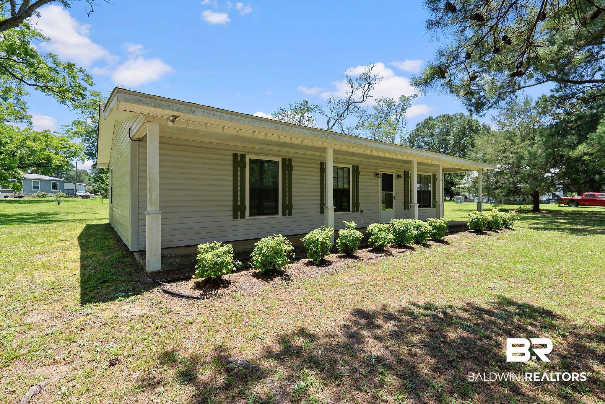 20540 Lacey Road Silverhill, AL 36576 - Photo 2 of 40 Single-story residence featuring light-toned siding, a full-length covered porch supported by white columns, and dark green louvered shutters
