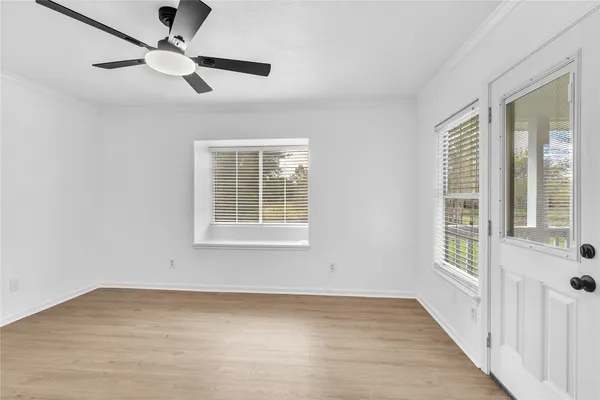 an empty room with wooden floor fan and windows