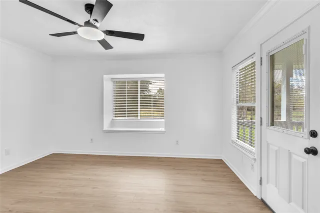 an empty room with wooden floor fan and windows