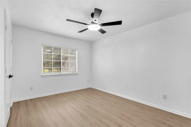 an empty room with wooden floor ceiling fan and windows