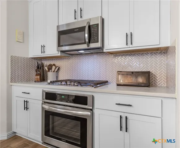 a kitchen with granite countertop white cabinets stainless steel appliances and wooden floor