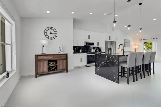 a kitchen with stainless steel appliances kitchen island granite countertop a stove a sink a dining table and chairs with white cabinets