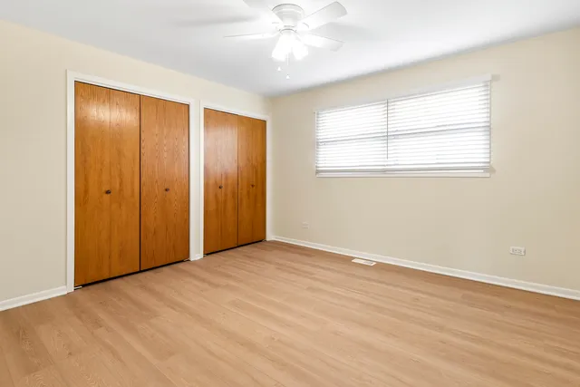 an empty room with wooden floor chandelier fan and windows