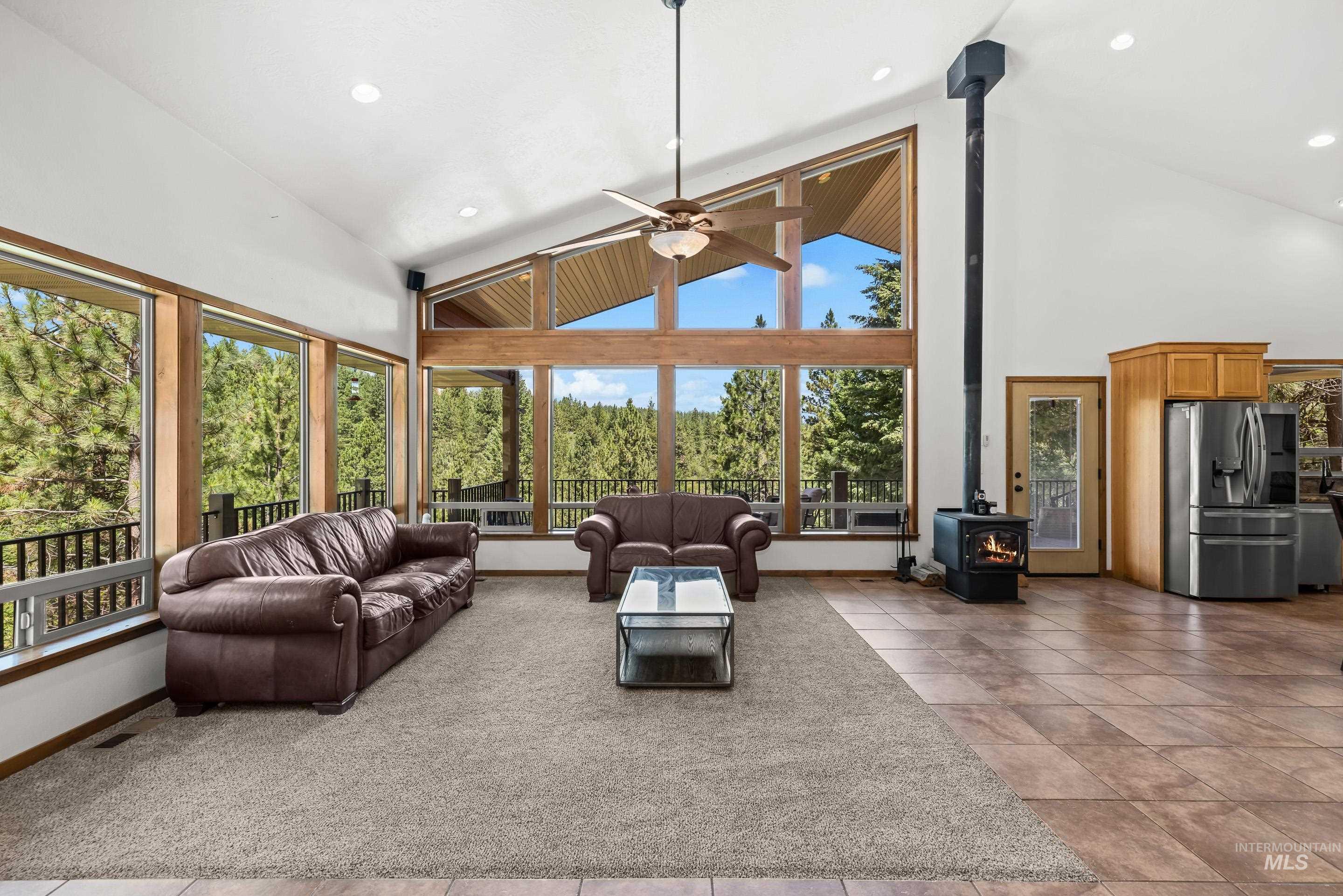 92 Cruickshank Road Horseshoe Bend, ID 83629 - Photo 7 of 50 Vaulted ceilings with ceiling fan in a spacious room featuring a wood-burning stove and extensive window walls
