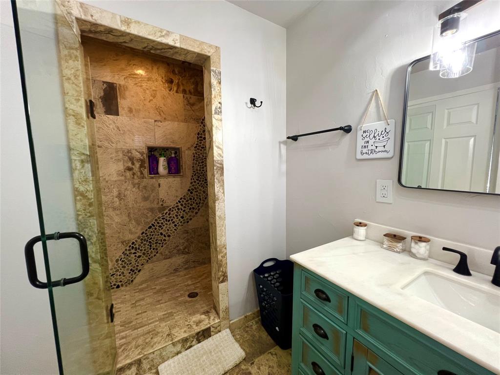 1017 Airport Road Graford, TX 76449 - Photo 21 of 32 a bathroom with a granite countertop sink a mirror a vanity and shower