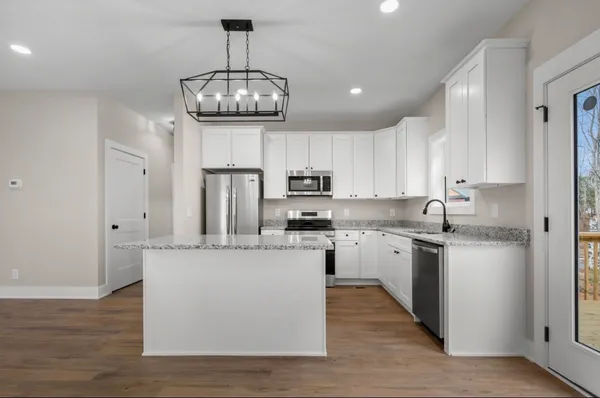 a kitchen with stainless steel appliances granite countertop a refrigerator a stove a sink and white cabinets