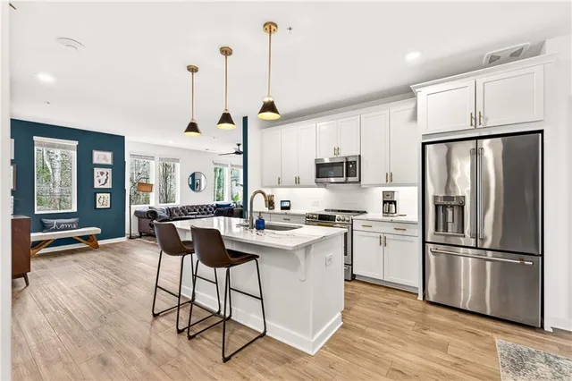 a kitchen with stainless steel appliances kitchen island a refrigerator a stove a dining table and chairs with wooden floor