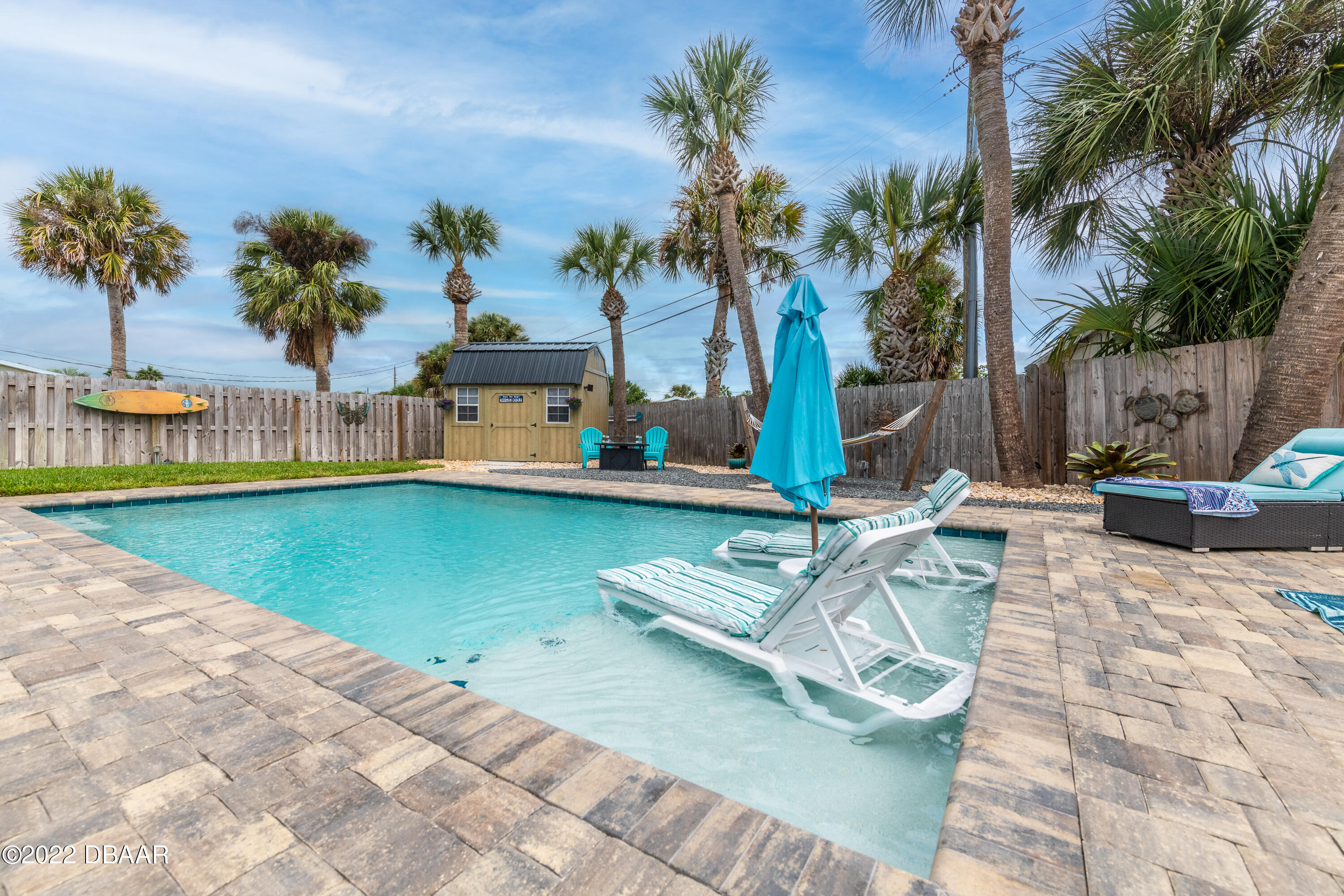 1253 Riverbreeze Boulevard Ormond Beach, FL 32176 - Photo 14 of 39 a view of a swimming pool with a lawn chairs under palm trees