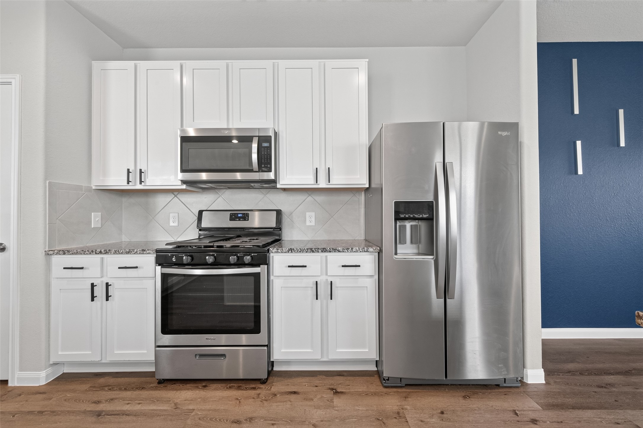 2526 Sturgeon Way Conroe, TX 77384 - Photo 4 of 49 This modern kitchen features sleek stainless steel appliances, including a oven, and microwave. It has white cabinetry, granite countertops, and a stylish tiled backsplash, all complemented by a rich wood floor.