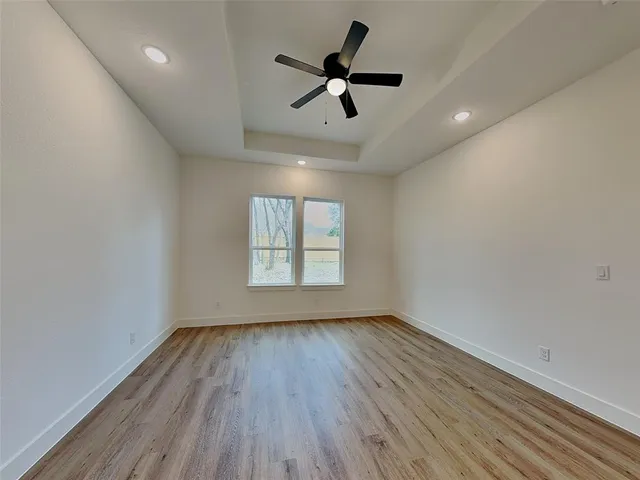 an empty room with wooden floor fan and windows