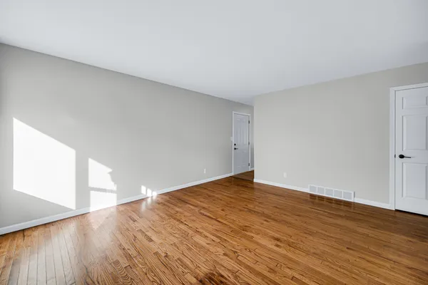 a view of an empty room with wooden floor and a window