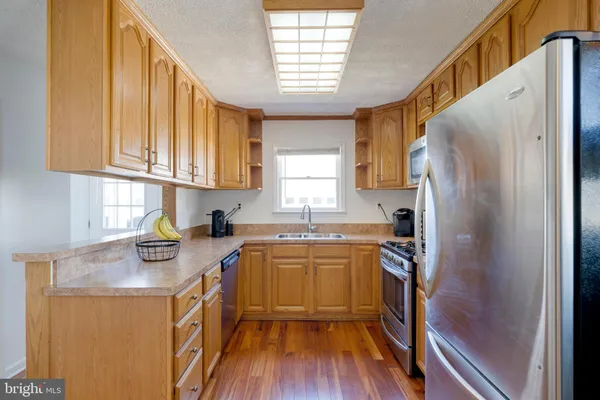 a kitchen with stainless steel appliances granite countertop a refrigerator a sink dishwasher a stove and white countertops with wooden floor