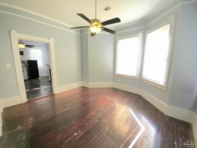 an empty room with wooden floor fan and windows
