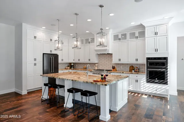 a kitchen with stainless steel appliances kitchen island granite countertop a stove top oven a refrigerator a sink and a dining table with wooden floor