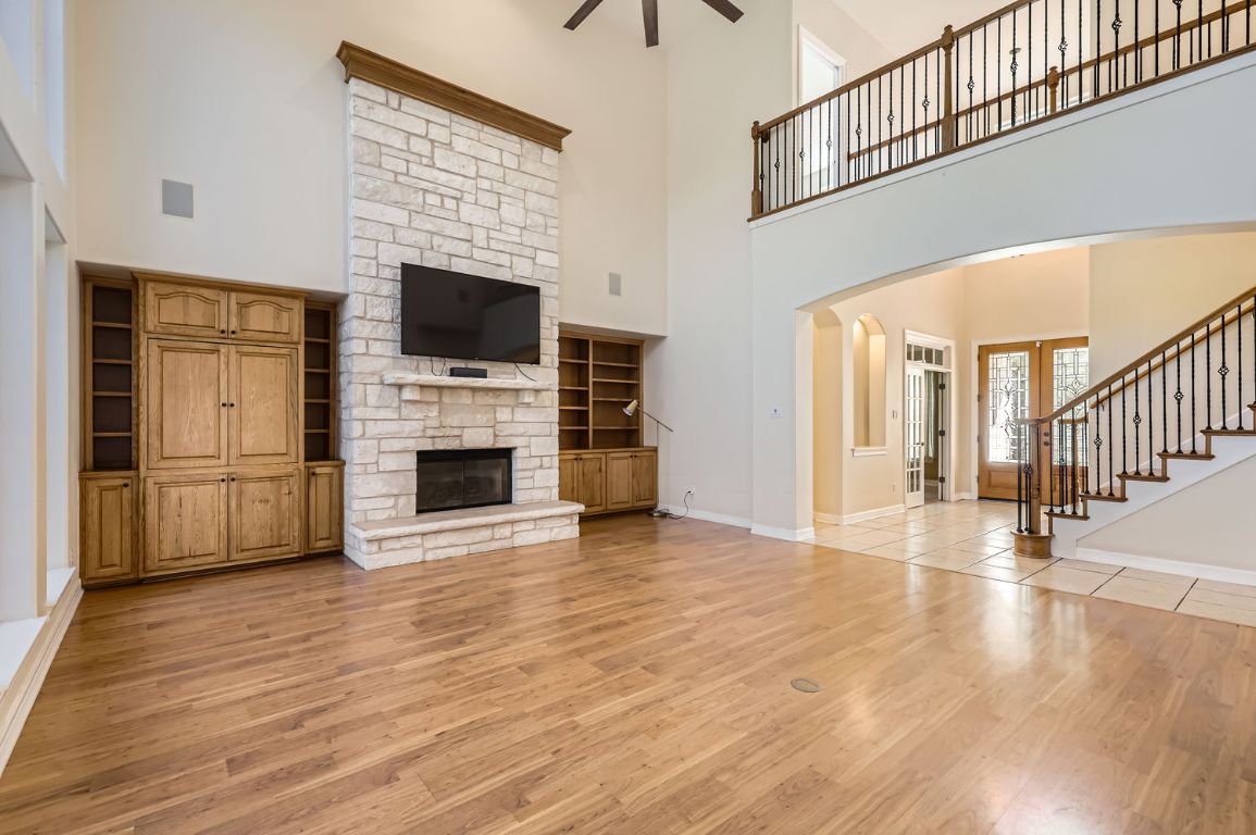 210 Amandas Way Leander, TX 78641 - Photo 6 of 38 Unfurnished living room featuring light wood finished floors, stairway, a ceiling fan, a stone fireplace, and baseboards