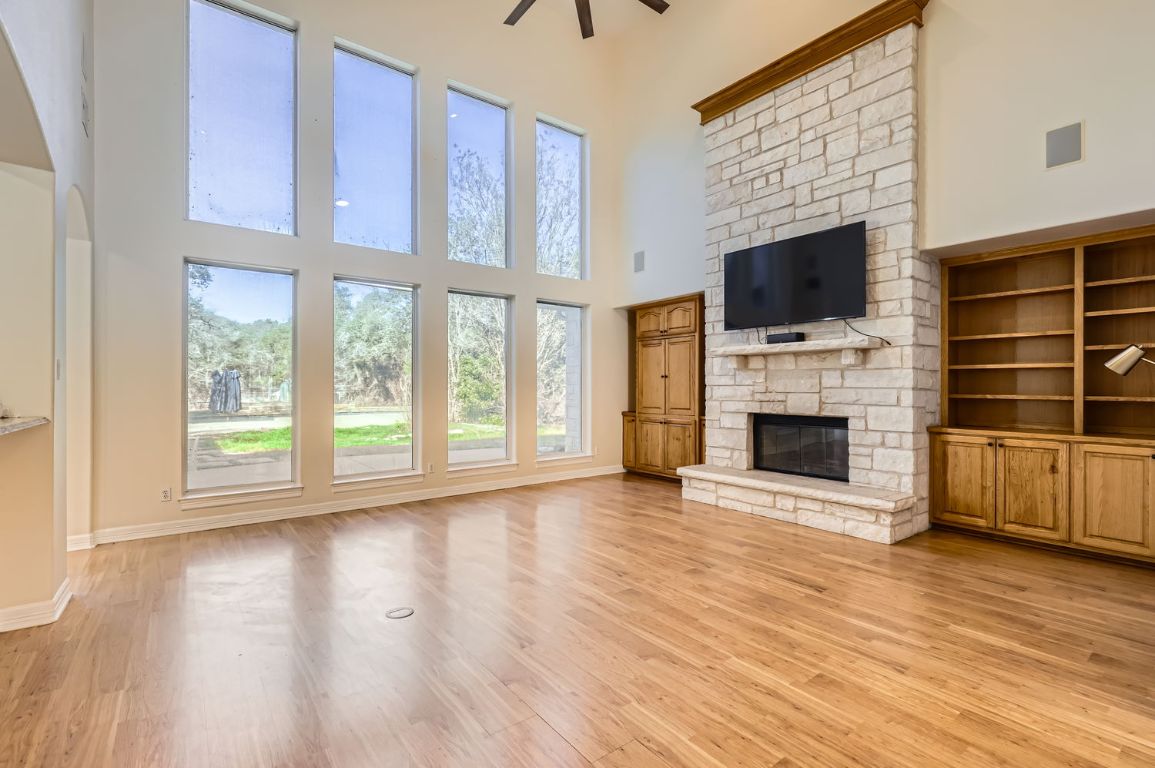 210 Amandas Way Leander, TX 78641 - Photo 7 of 38 Unfurnished living room featuring a ceiling fan, light wood-style flooring, a stone fireplace, and a towering ceiling