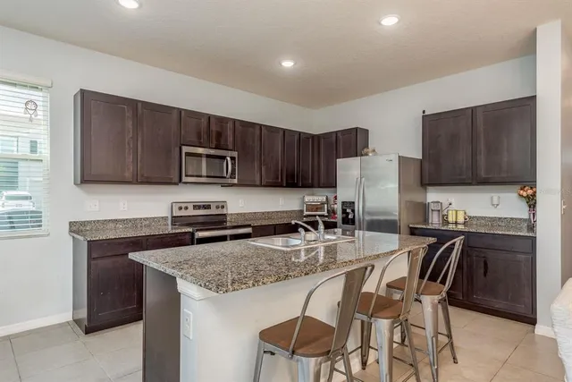 a kitchen with granite countertop stainless steel appliances a stove a sink a microwave a refrigerator and cabinets