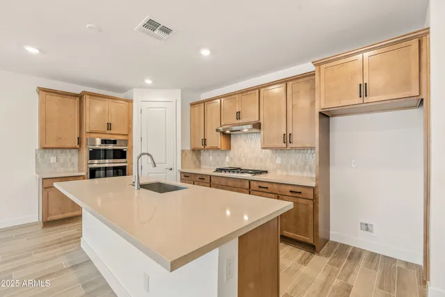 a large kitchen with kitchen island a stove a sink a refrigerator and white cabinets with wooden floor