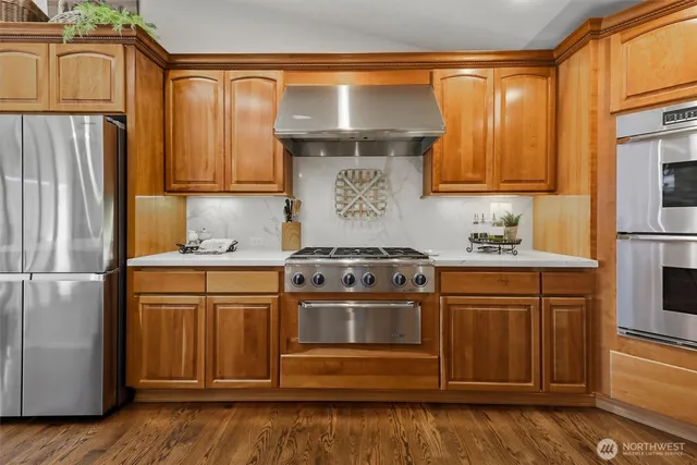 a kitchen with stainless steel appliances granite countertop a refrigerator a stove and a sink with wooden floors