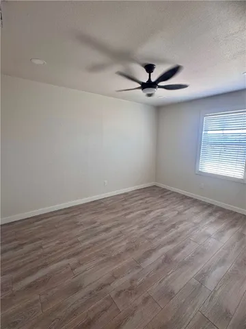 an empty room with wooden floor ceiling fan and windows