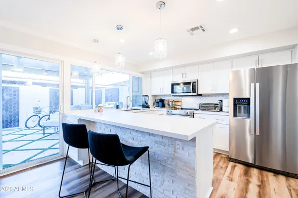 a kitchen with stainless steel appliances granite countertop a refrigerator a sink dishwasher a stove and white cabinets with wooden floor