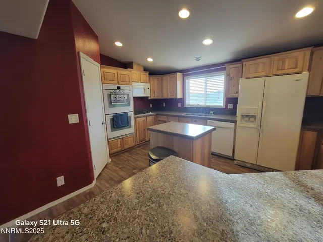 a kitchen with stainless steel appliances granite countertop a refrigerator a sink a stove a microwave oven with white cabinets and wooden floor