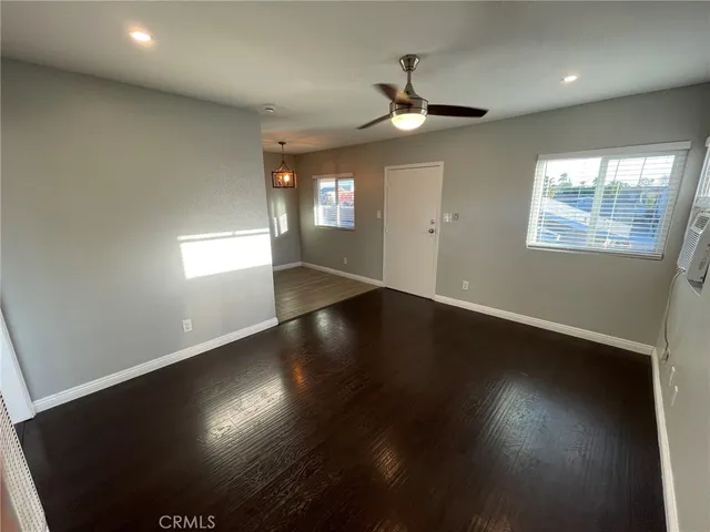 an empty room with wooden floor chandelier fan and windows