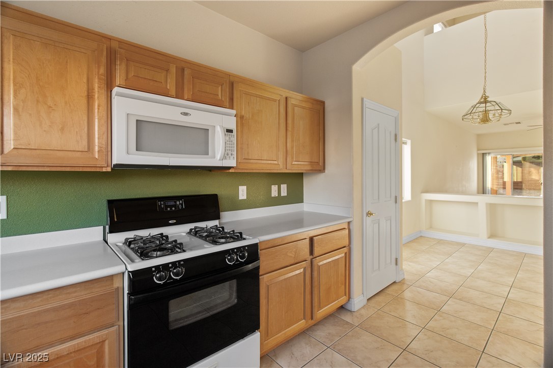 2715 Brinkley Manor Street Laughlin, NV 89029 - Photo 17 of 89 Kitchen with gas range, white microwave, light countertops, hanging light fixtures, and light tile patterned floors