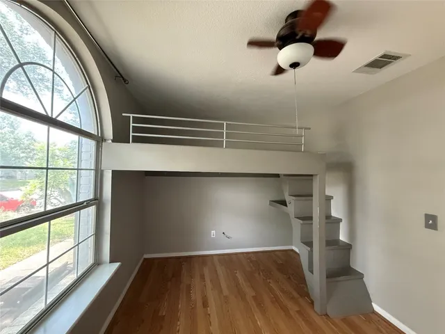 a view of empty room with wooden floor and fan
