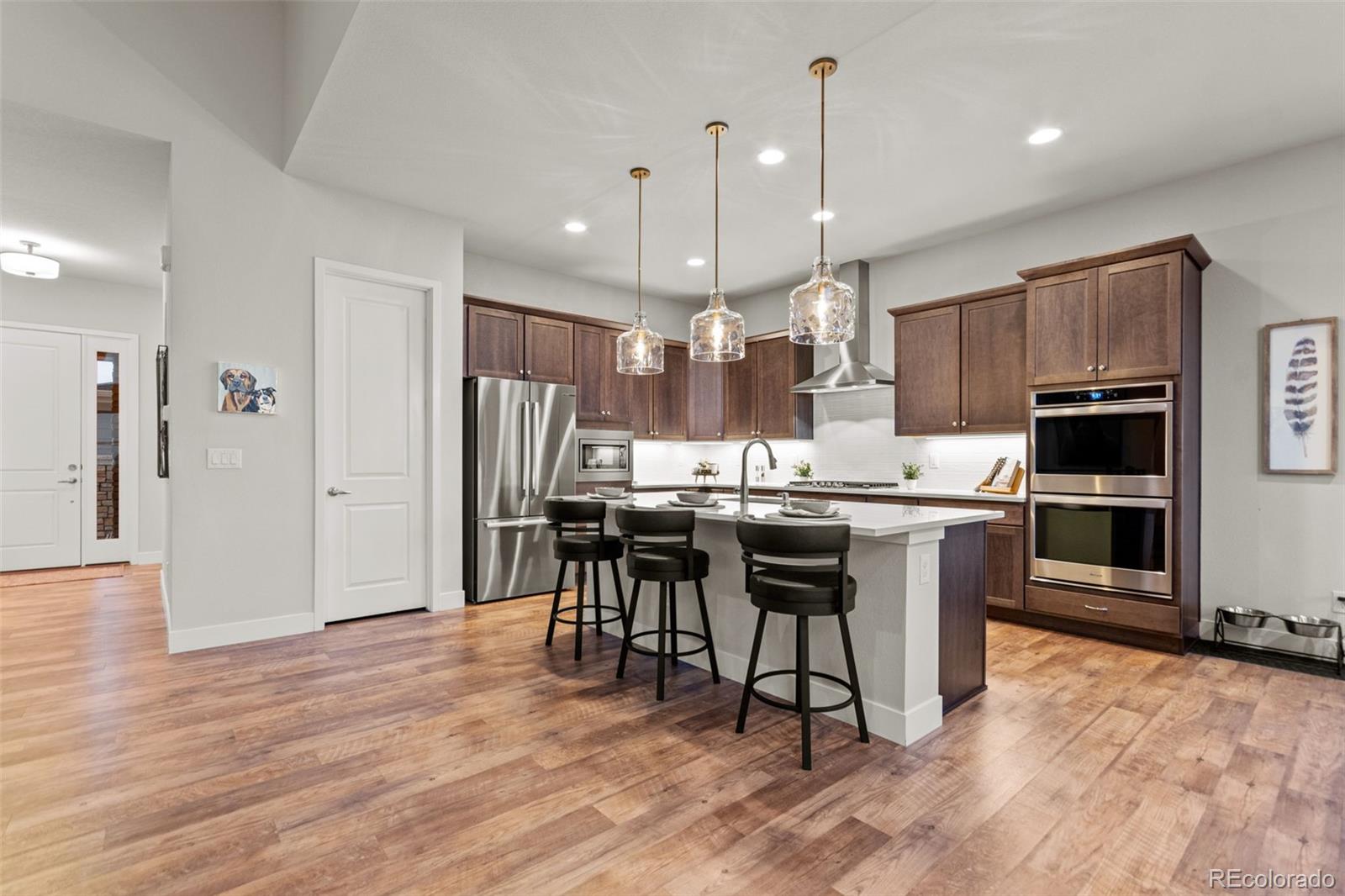 9388 Dunraven Loop Arvada, CO 80007 - Photo 8 of 50 a kitchen with stainless steel appliances kitchen island granite countertop a refrigerator a stove a sink a dining table and chairs with wooden floor