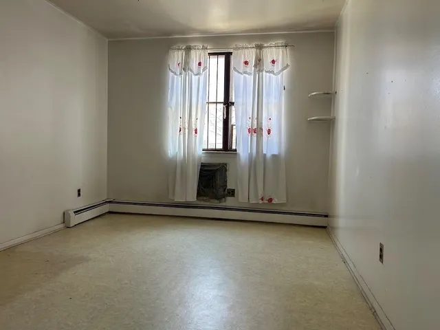 a view of an empty room with a kitchen and a refrigerator
