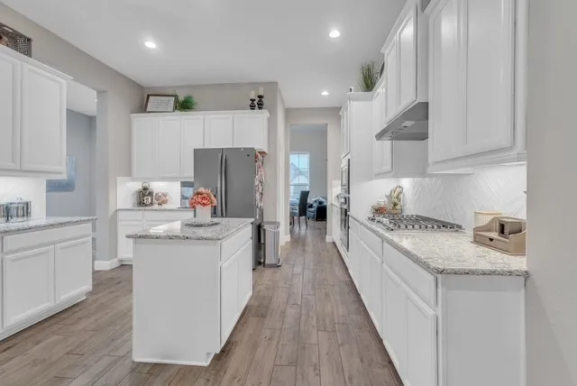 a kitchen with granite countertop a sink stove refrigerator and white cabinets with wooden floor
