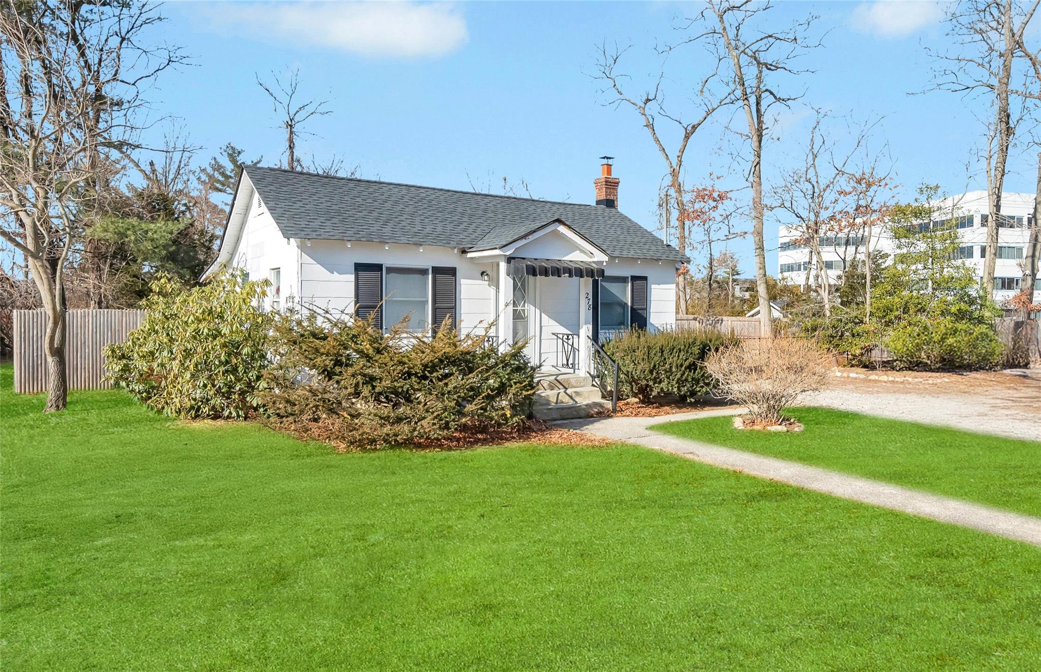 View of front of property featuring a shingled roof, fence, dirt driveway, a chimney, and a front yard