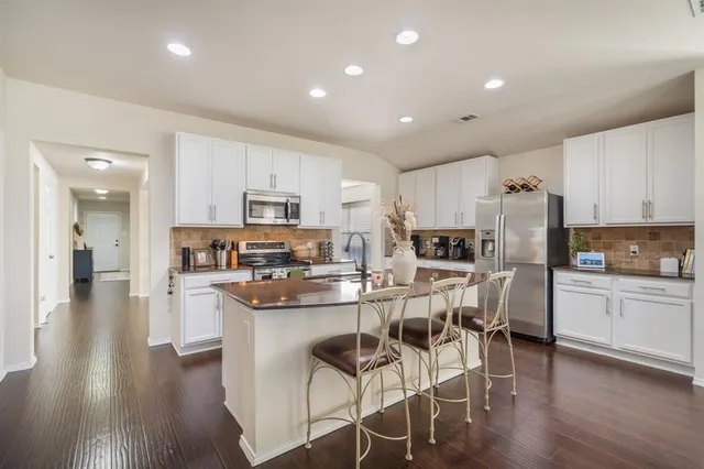 a kitchen with stainless steel appliances granite countertop a refrigerator a stove top oven a sink dishwasher and white cabinets with wooden floor