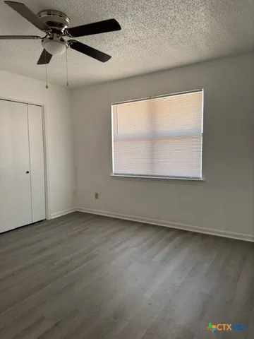 an empty room with wooden floor fan and windows
