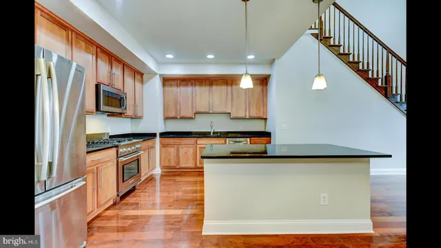 a kitchen with stainless steel appliances granite countertop a refrigerator a stove and a sink with wooden floor