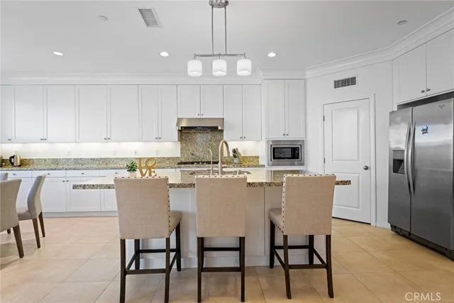 a kitchen with kitchen island granite countertop a dining table chairs refrigerator and cabinets