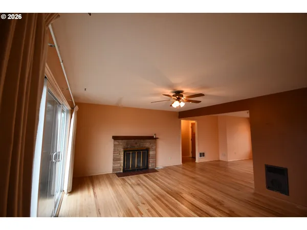 a view of an empty room with wooden floor fireplace and a window