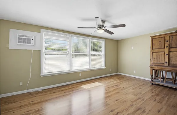 an empty room with wooden floor chandelier fan and windows