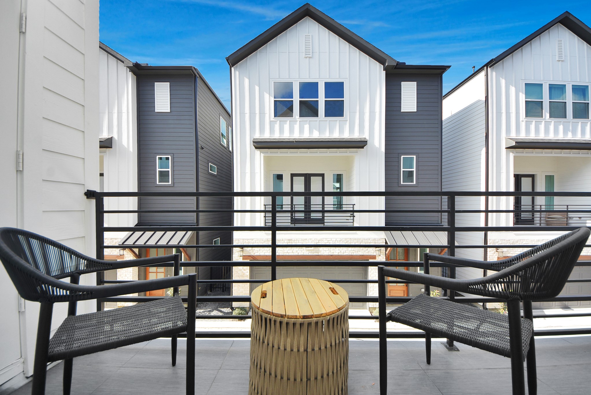 927 Fisher Street, Unit B Houston, TX 77018 - Photo 38 of 47 Step out onto this modern balcony with sleek black railings and outdoor seating, overlooking contemporary townhouses with contrasting exteriors. The space is perfect for relaxing and enjoying neighborhood views under a clear blue sky.