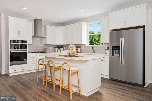 a kitchen with stainless steel appliances granite countertop a refrigerator a sink a stove a dining table and chairs with wooden floor