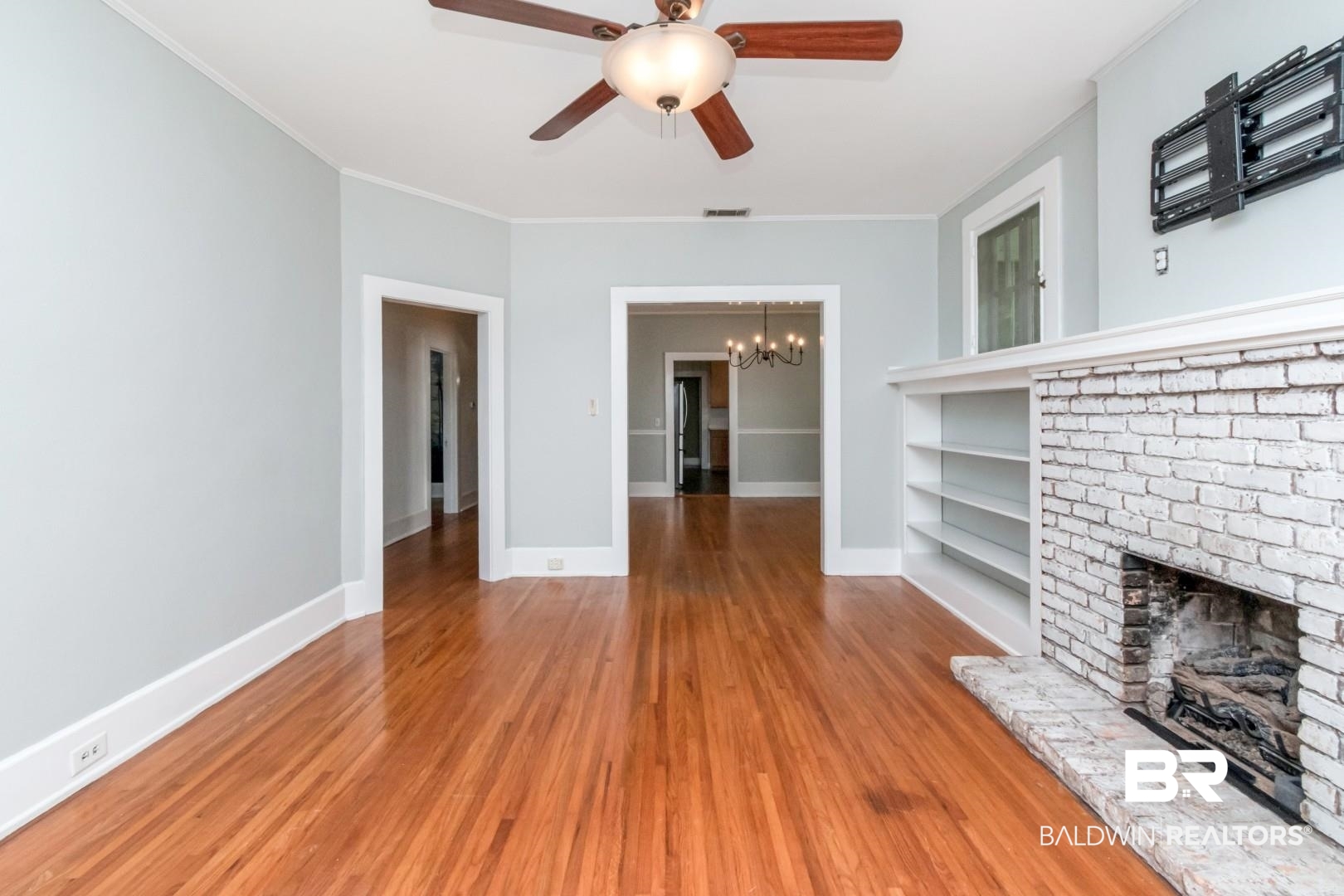 10 Macy Place Mobile, AL 36604 - Photo 6 of 43 Unfurnished living room featuring a chandelier, built in features, a brick fireplace, wood finished floors, and ceiling fan
